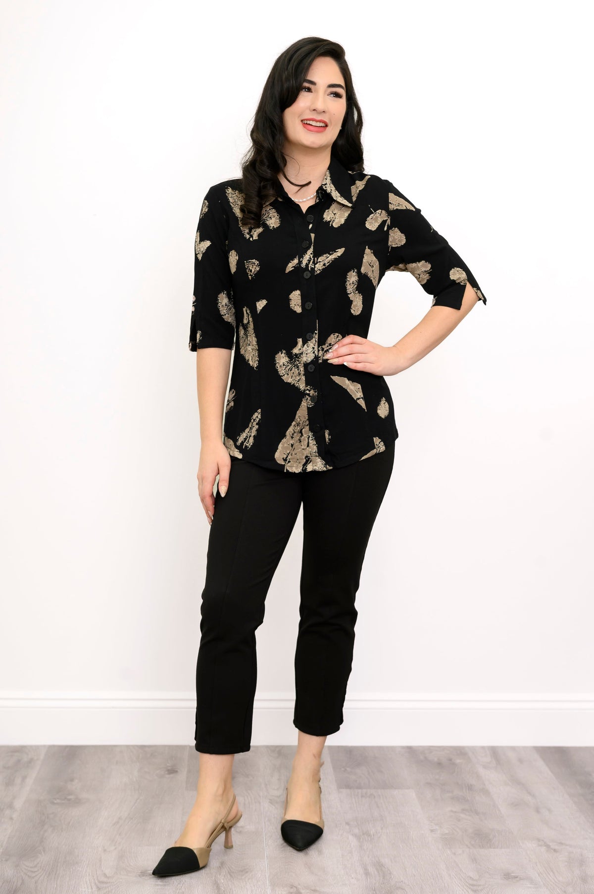 Woman wearing a black blouse with tan leaf pattern and black pants against a white background, front view