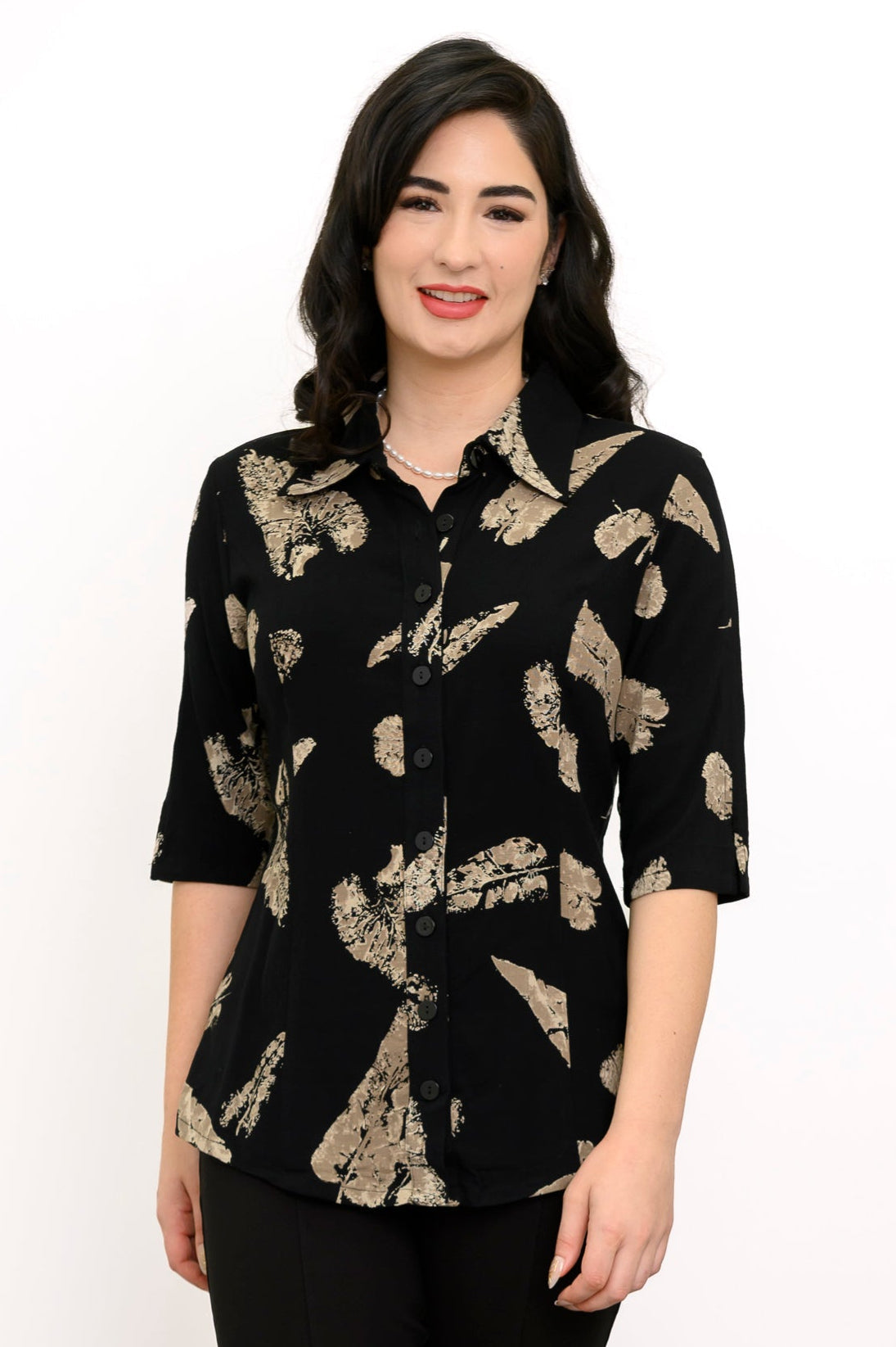Woman wearing a black blouse with tan leaf pattern and black pants against a white background, front view