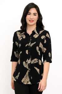 Woman wearing a black blouse with tan leaf pattern and black pants against a white background, front view