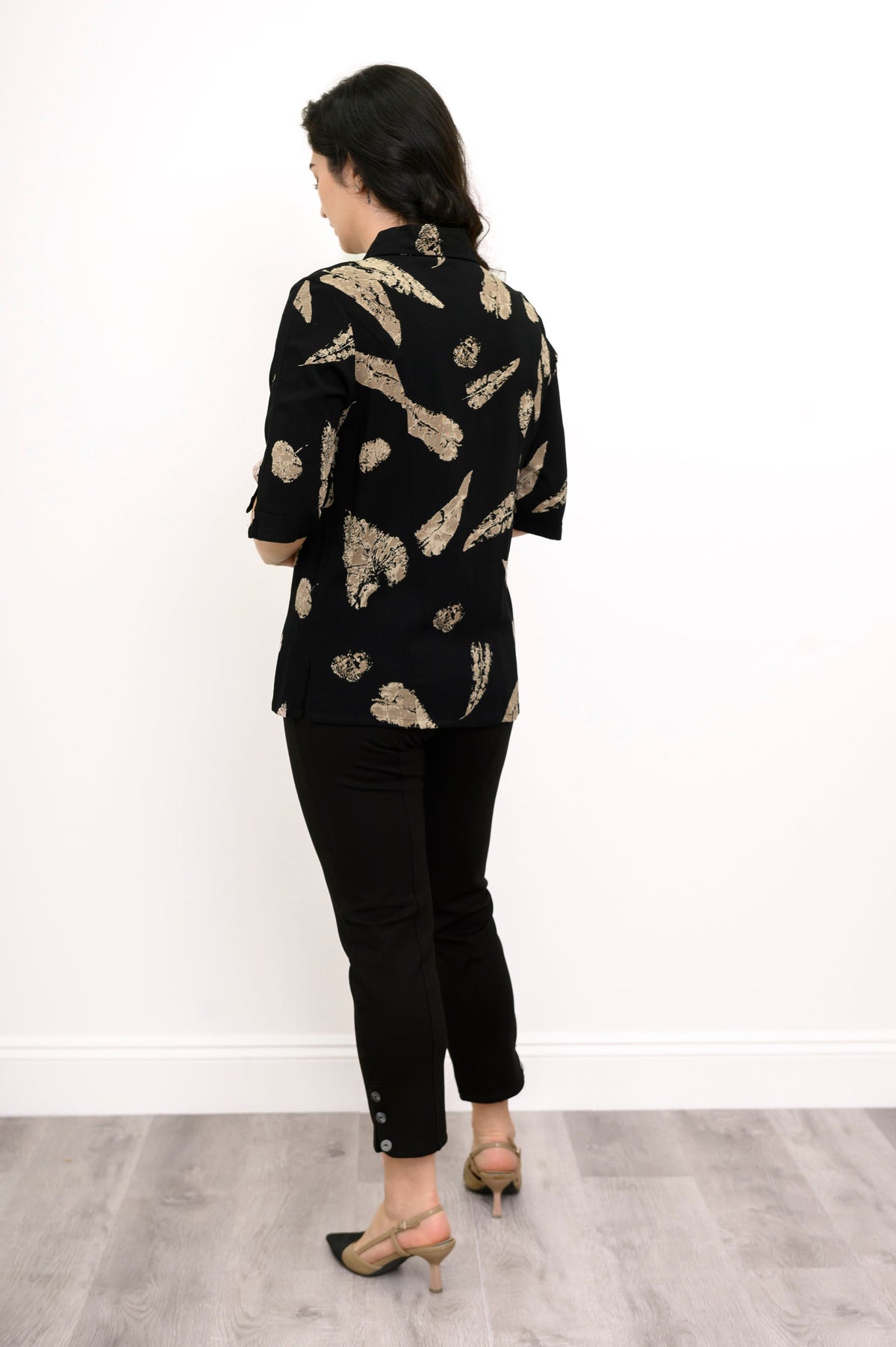 Back view of woman wearing a leaf print blouse and black pants against a white background