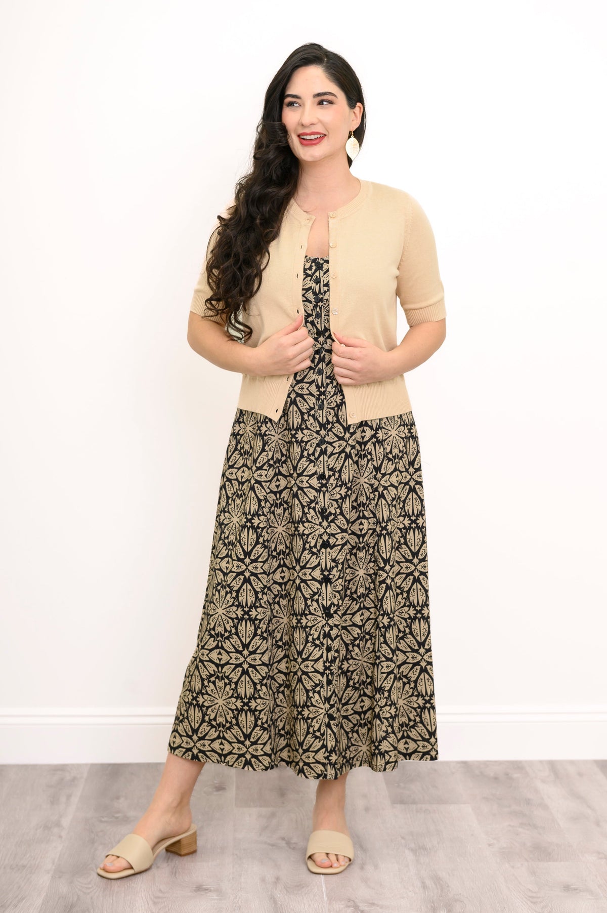 Full body front view of woman wearing unbuttoned beige cardigan and black an beige dress with button detail