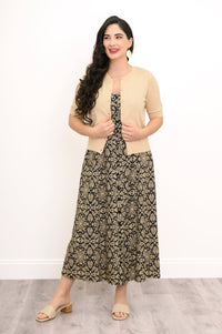 Full body front view of woman wearing unbuttoned beige cardigan and black an beige dress with button detail