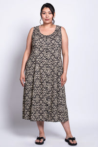 Front view of woman wearing round-neck sleeveless dress with button detail and neutral colored print