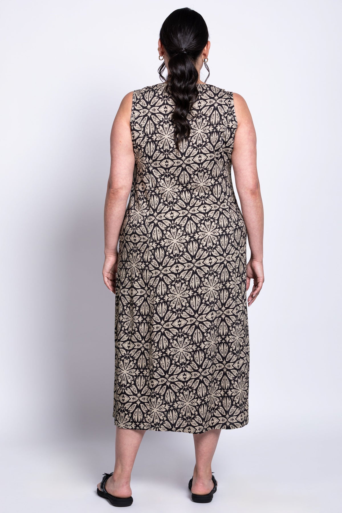 Back view of model wearing sleeveless long dress with black and beige floral geometric pattern
