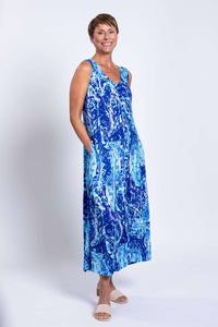 Woman posing in sleeveless blue printed maxi dress with hands in pockets