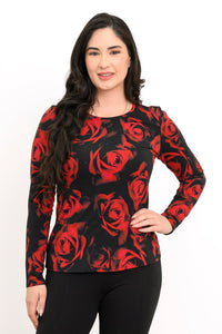Front view of a female model wearing a long sleeve black top with red roses with black pants, hand on hip, against a white backdrop