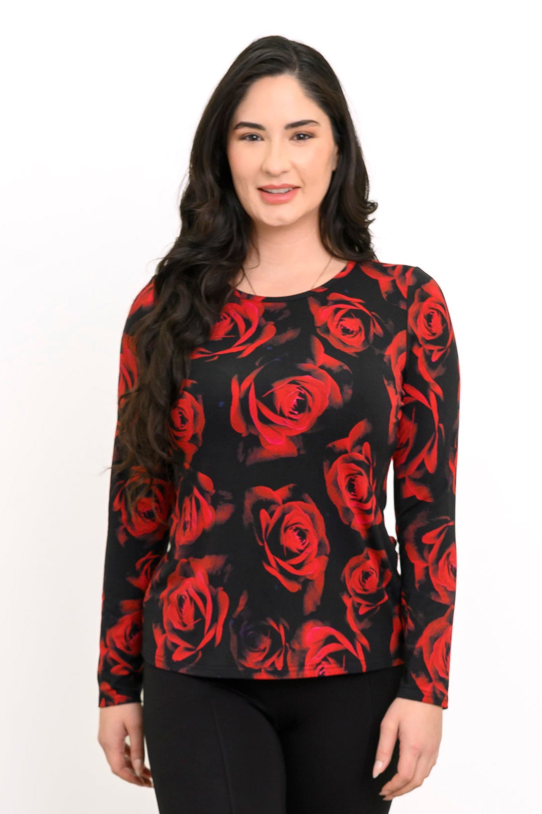 Front view of a female model wearing a long sleeve black top with red roses with black pants, against a white backdrop