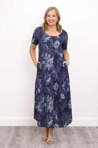 Front view of woman wearing long navy blue floral dress with pockets and sandals on a white background