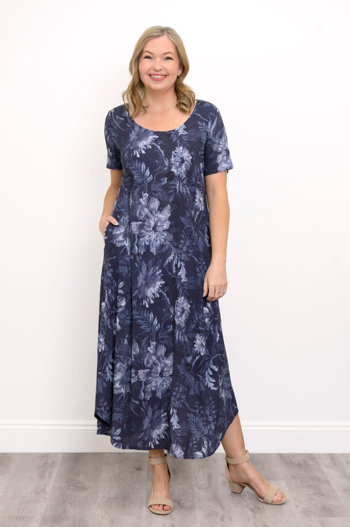 Front view of woman in scoop neck maxi dress with navy blue floral print and beige sandals