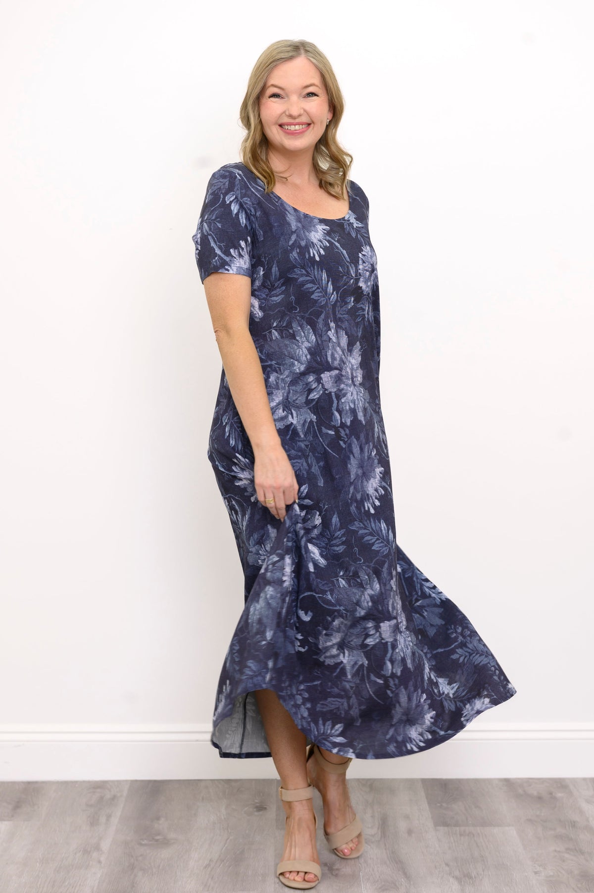 Front view of woman smiling and swaying her long dark blue botanical print dress