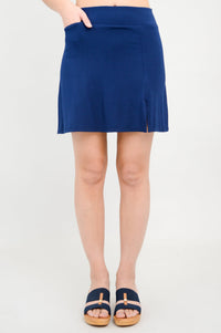 Close up front view of woman posing with her hand in her pocket wearing a deep blue mini skirt with slit detail