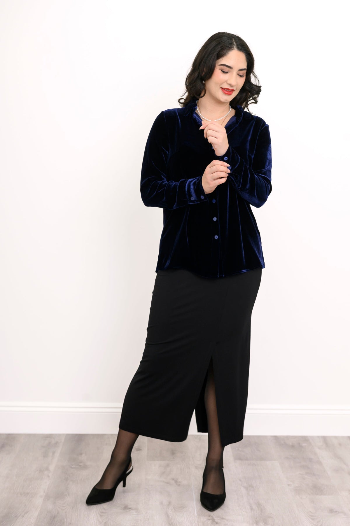 Straight-on full body portrait of an elegant navy blue silk velvet shirt styled with a black front-slit skirt