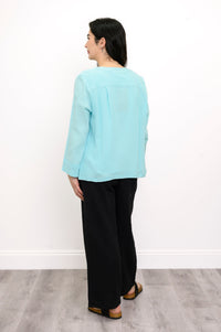 Woman wearing a light blue top and black pants on a white background, back view