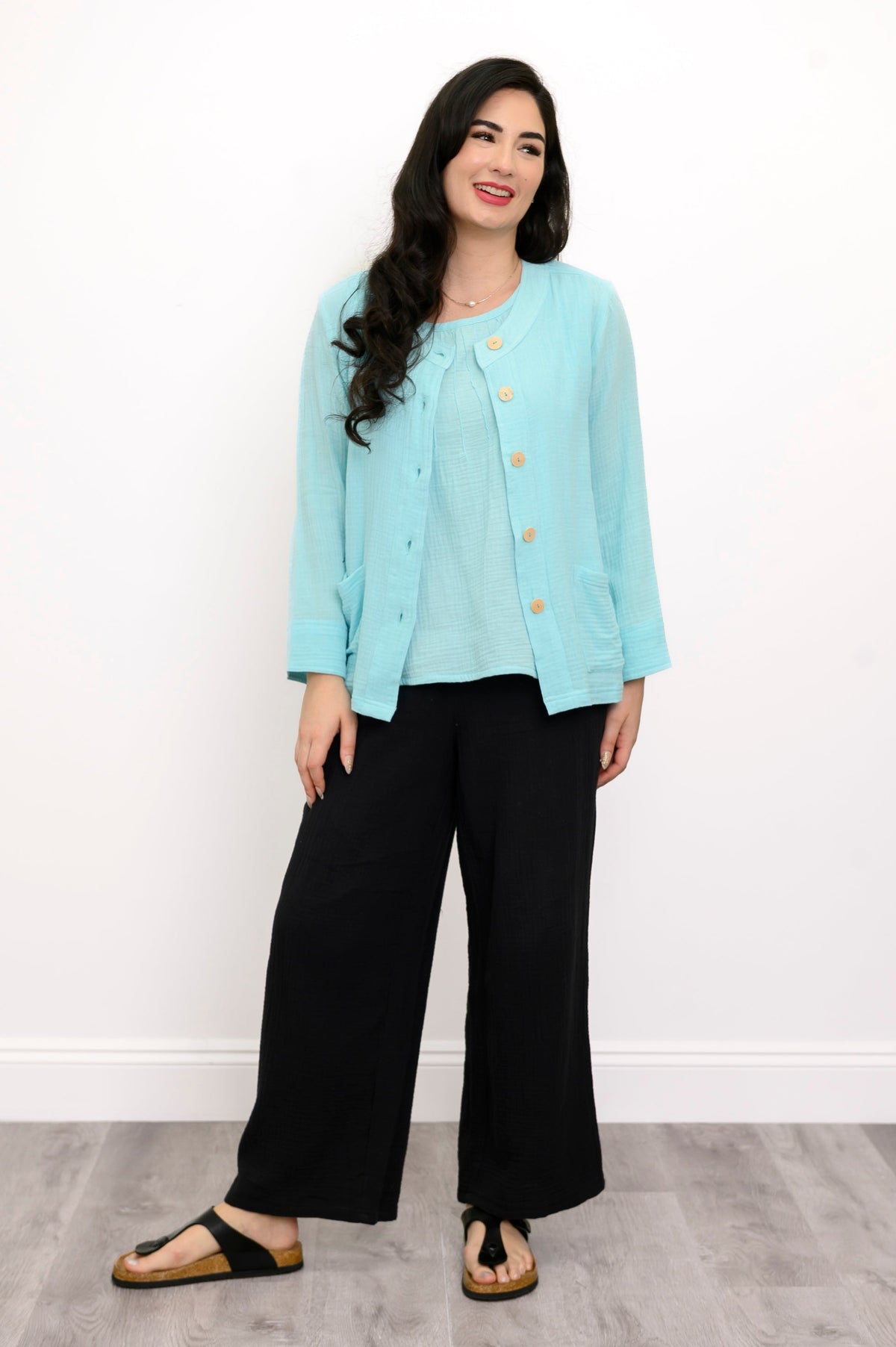 Woman wearing a light blue jacket on a light blue top and black pants on a white background, front view