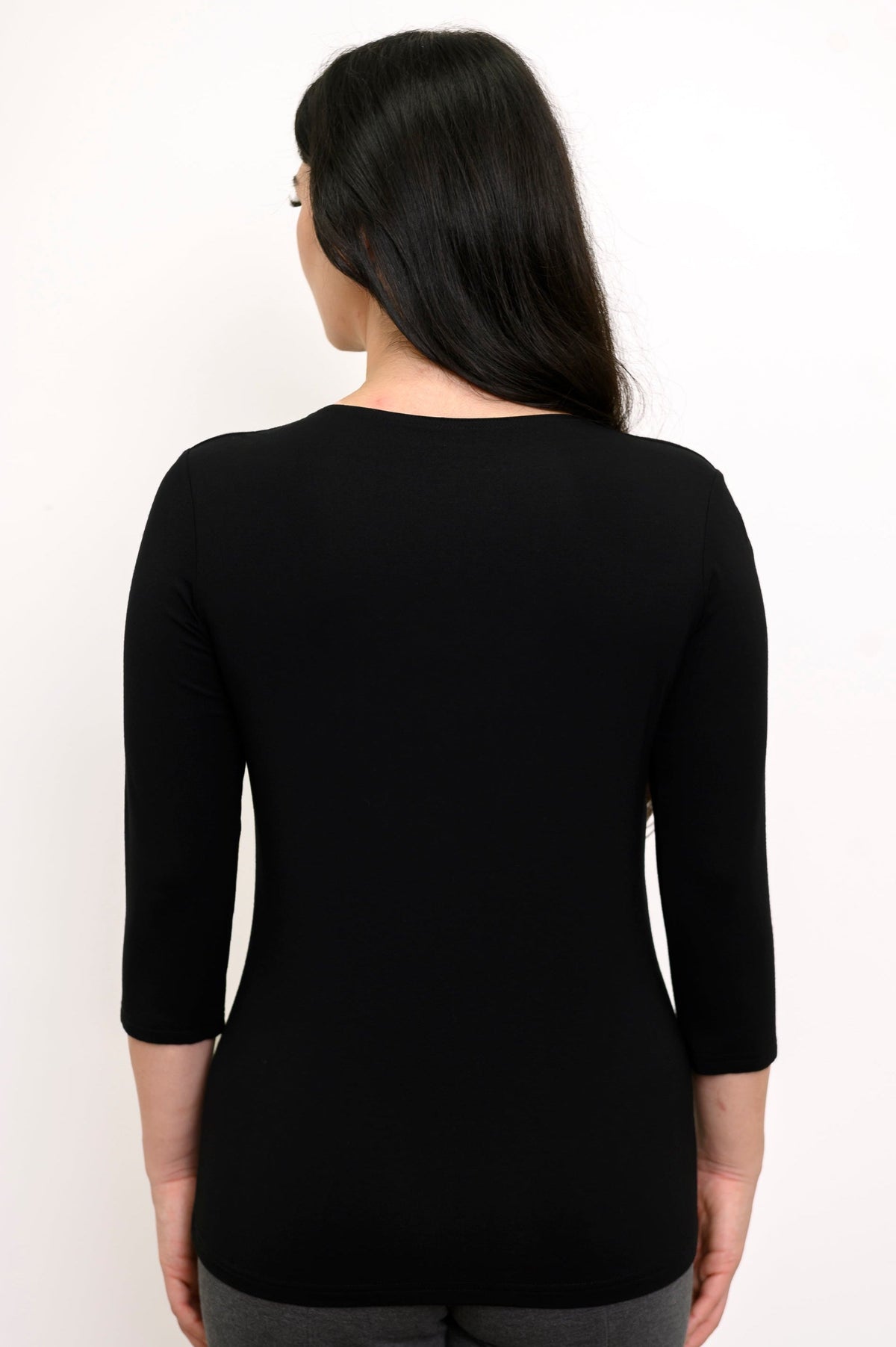 Back view of model wearing a black 3/4 sleeve top and grey pants against a white background
