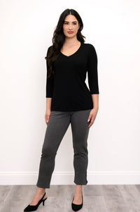 Full body view of woman with her hands at her side wearing a black top and grey slim fit pants