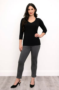 Woman posing with her hand on her hip while wearing a black v-neck shirt, grey pants, and black pumps