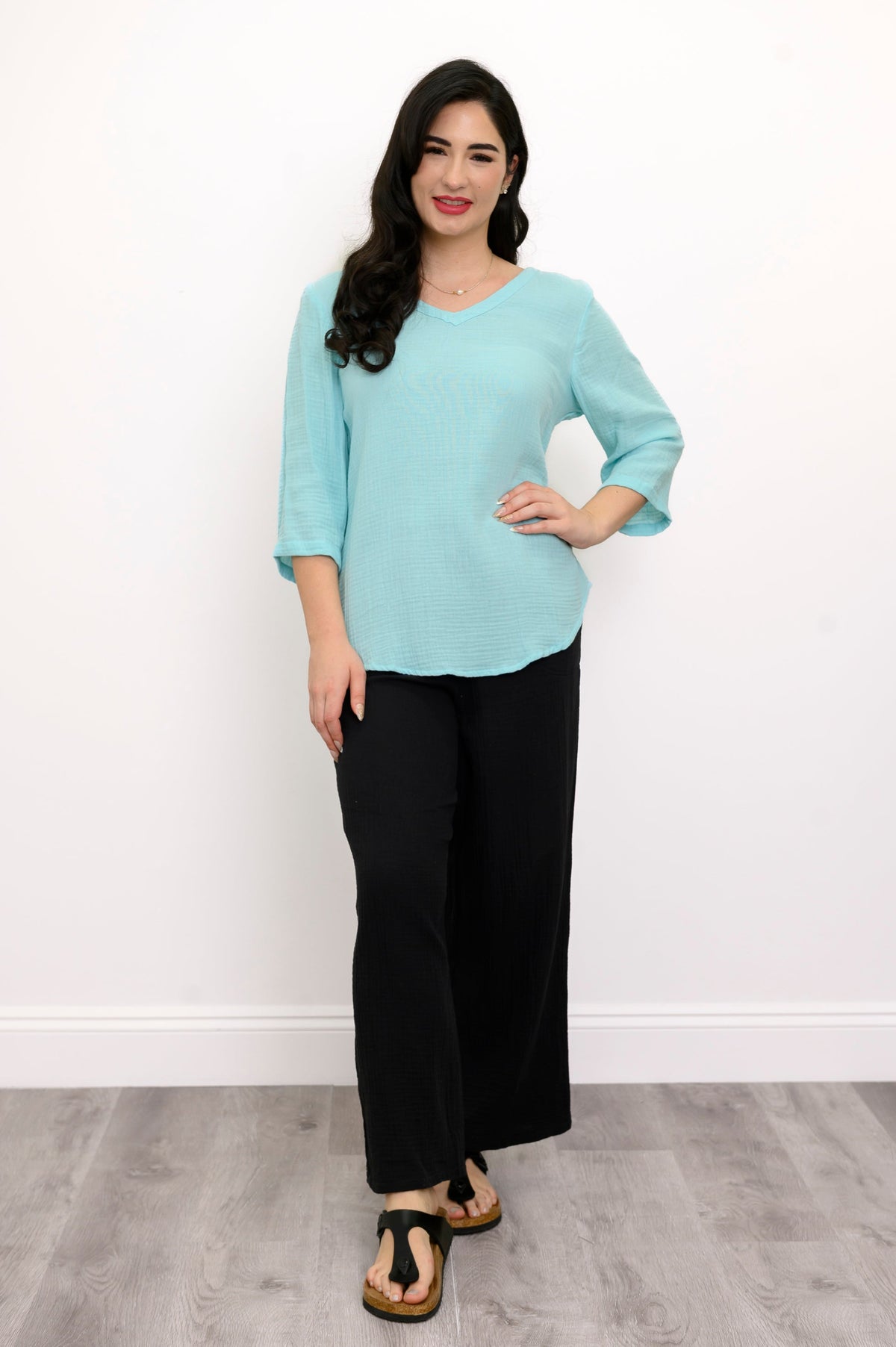 Woman wearing a light blue top, black pants, and black sandals against a white background, front view