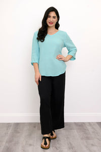 Woman wearing a light blue top, black pants, and black sandals against a white background, front view
