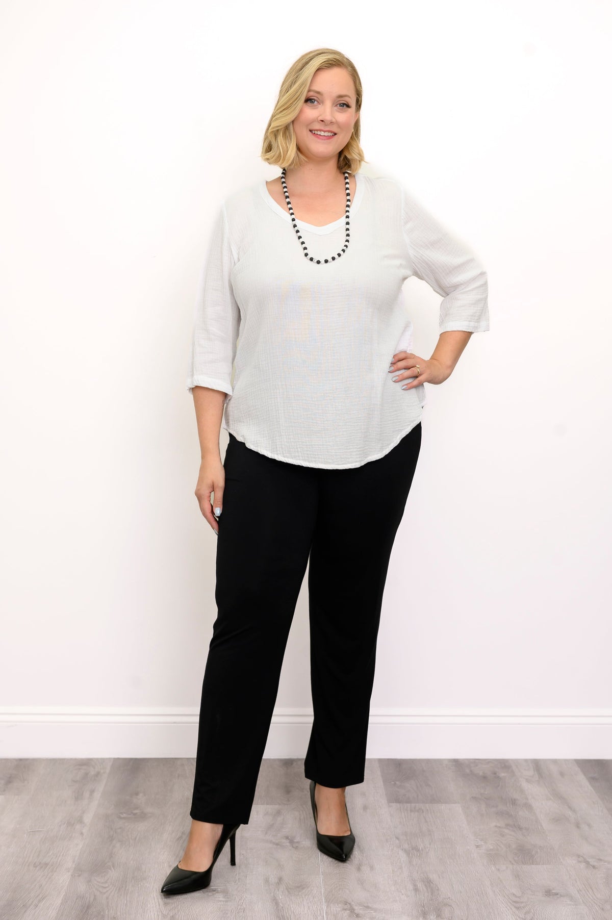 Woman wearing a white blouse, black pants, and black shoes against a white background, front view