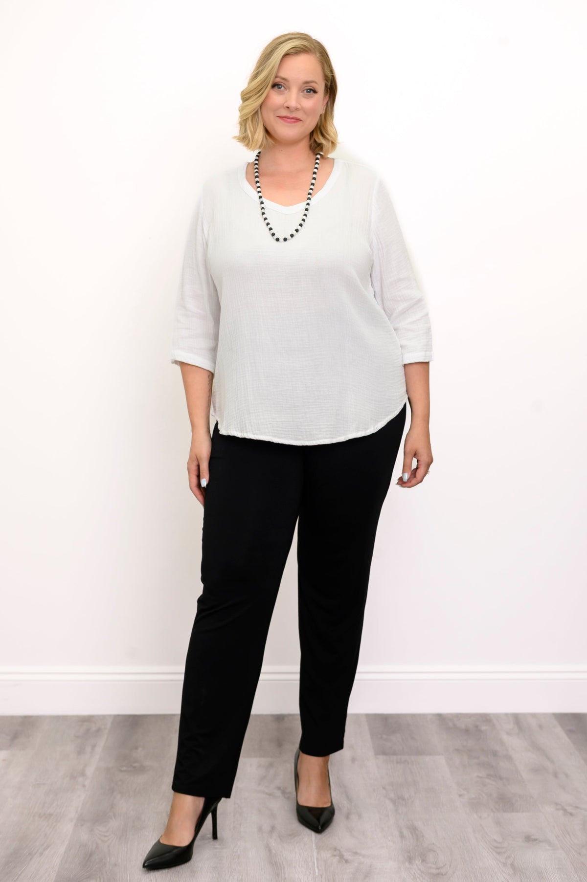 Woman wearing a white blouse, black pants, and black shoes against a white background, front view