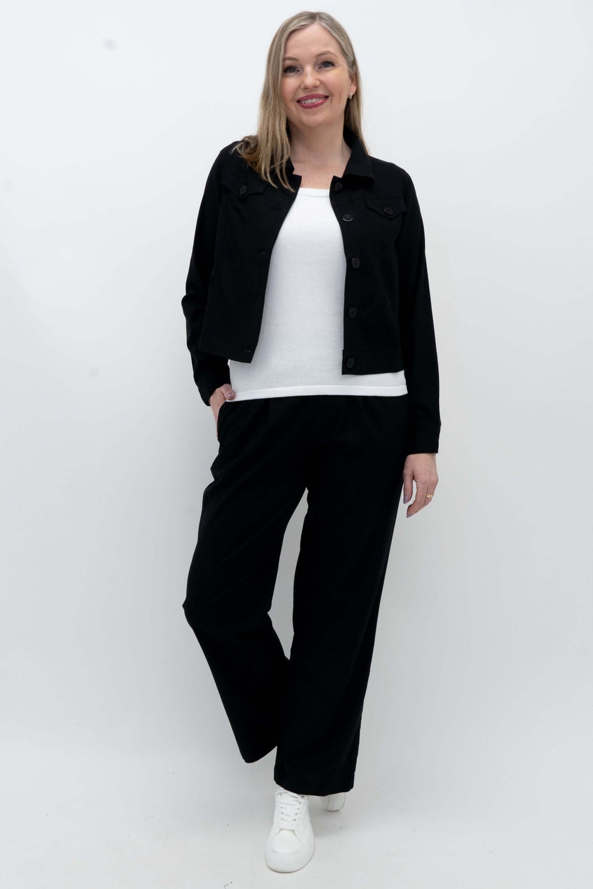Model posing in black jacket on a white tee, styled with black wide-leg pants, hand in pocket