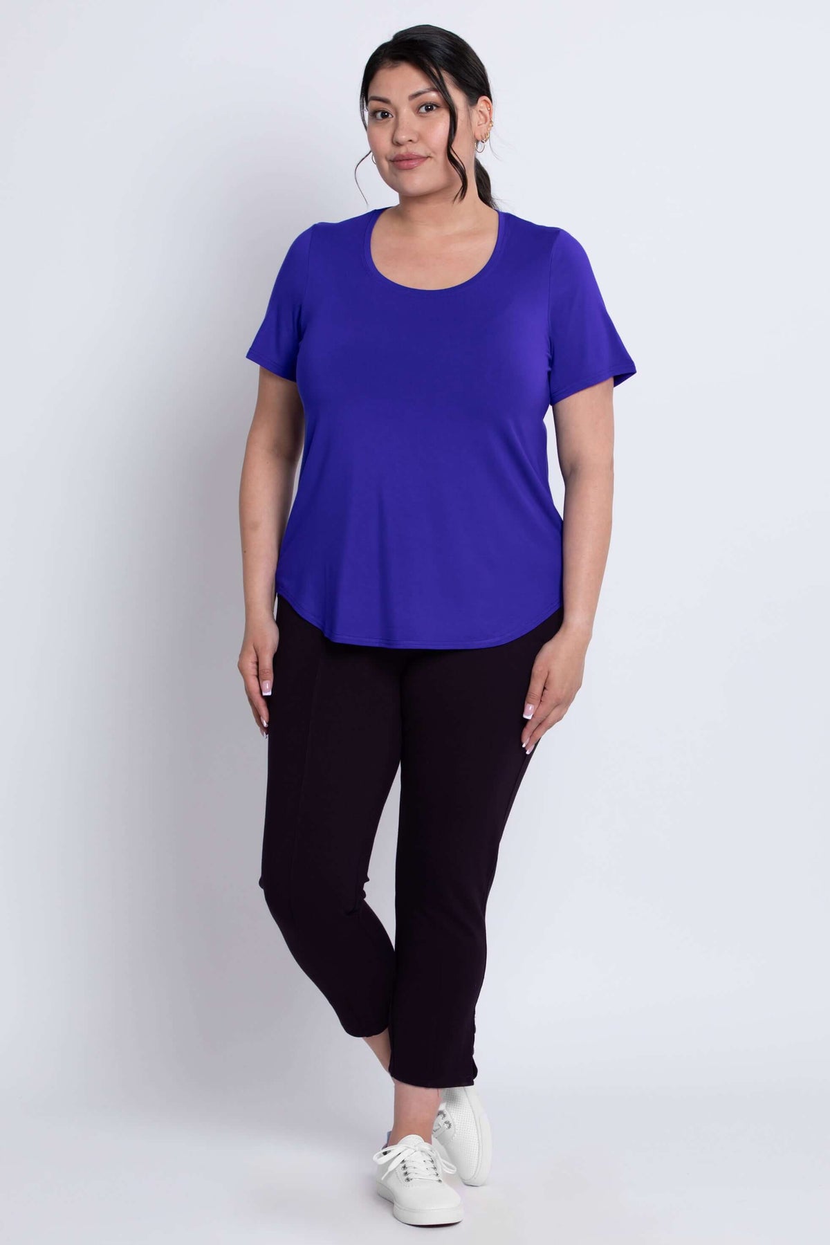 Woman standing in a purple scoop neck tee and dark cropped pants, front angle