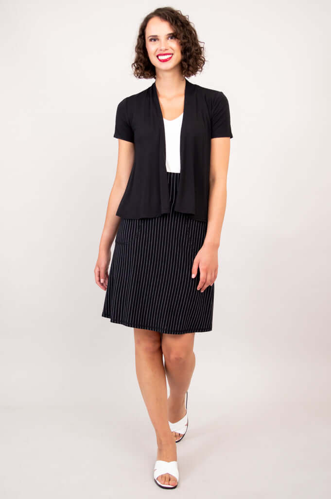 Woman walking forward wearing a black open short sleeve jacket and striped skirt