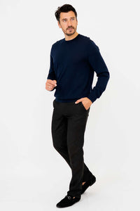 Man in navy sweater and black pants posing with one hand in pocket, walking forward