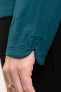 Close-up of a person's hand wearing a teal long-sleeve top with a small side slit near the cuff, paired with black pants