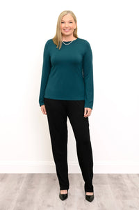 Front view of a female model wearing a teal long sleeve top with black pants and shoes, against a white wall and gray floor