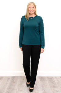 Front view of a female model in walking pose wearing a teal long sleeve top with black pants and shoes, against a white wall and gray floor