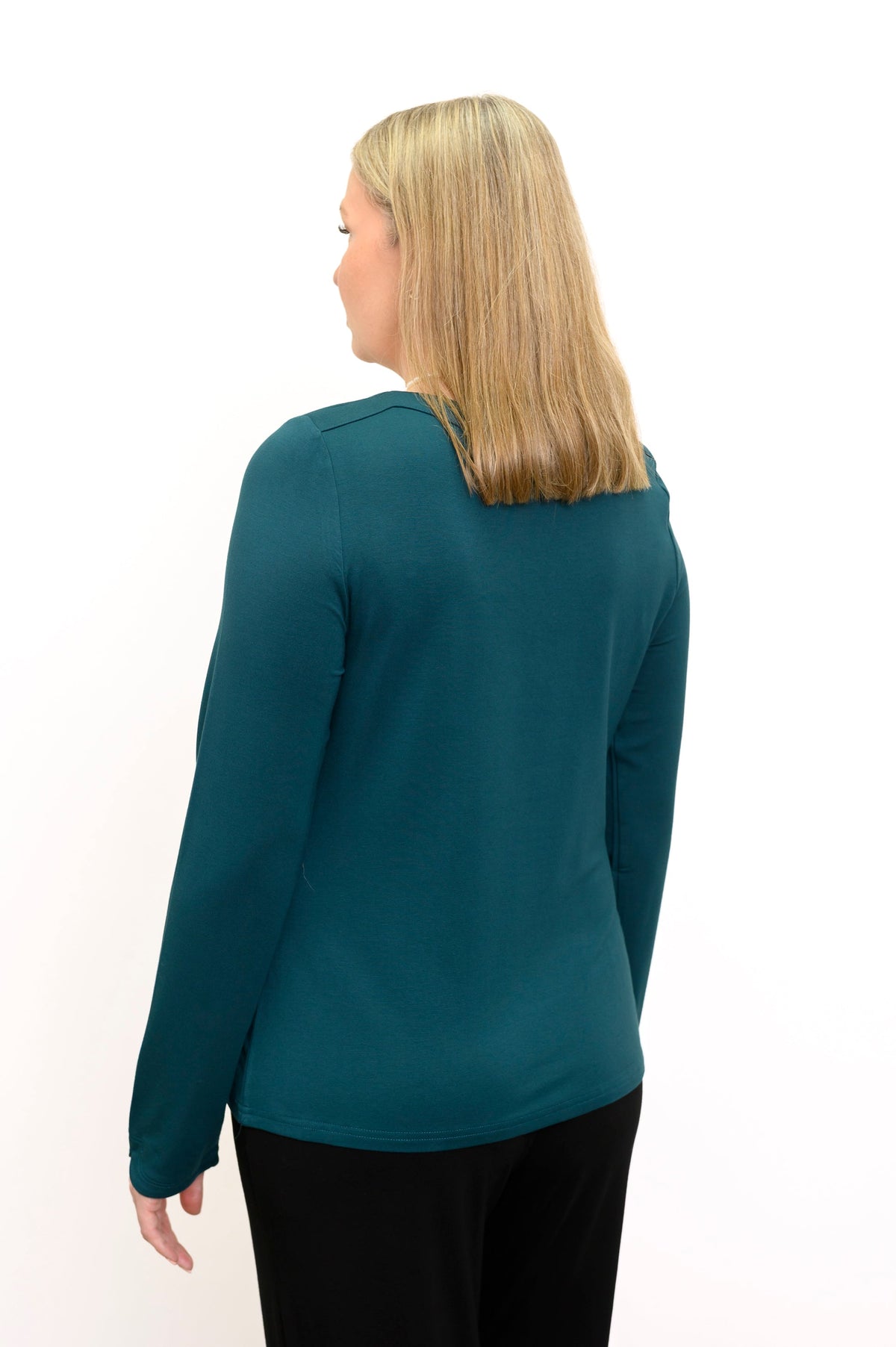 Back view of a female model wearing a teal long sleeve top with black pants, against a white backdrop
