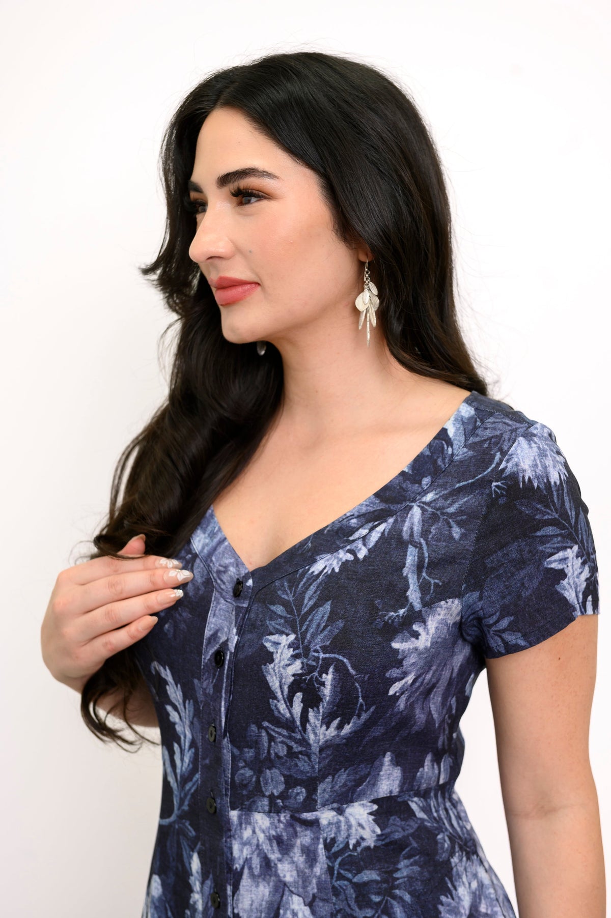 Close up view of woman facing to the side and wearing a silver v-neck short sleeve dress with a dark navy floral print