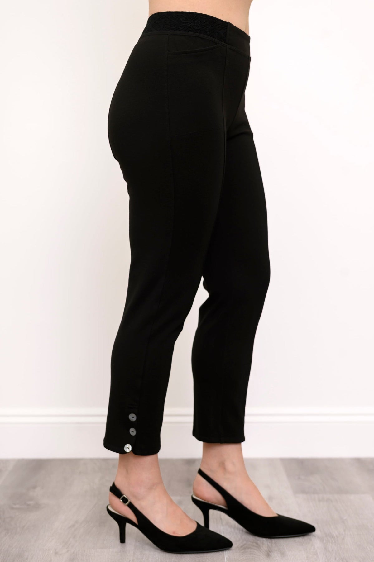 Side view of highwaisted black pants with elastic waistband and button detail at the hem