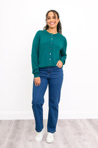 Woman modeling a casual emerald green buttoned knit sweater paired with denim pants on white.