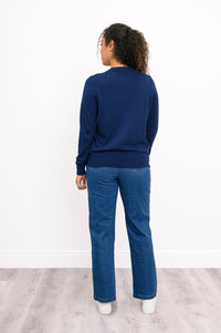 Back view of a woman wearing a hip length navy blue cotton viscose knit cardigan and denim jeans.