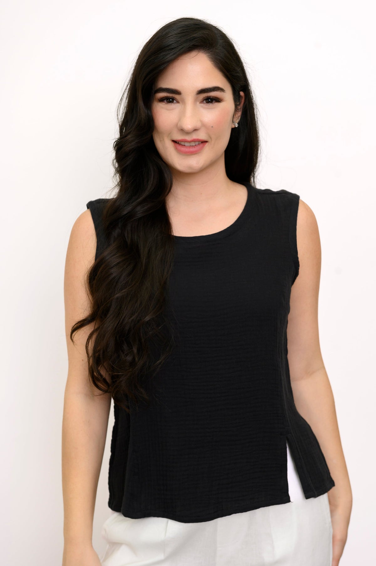 Woman wearing a black sleeveless top and white pants against a white background, front view