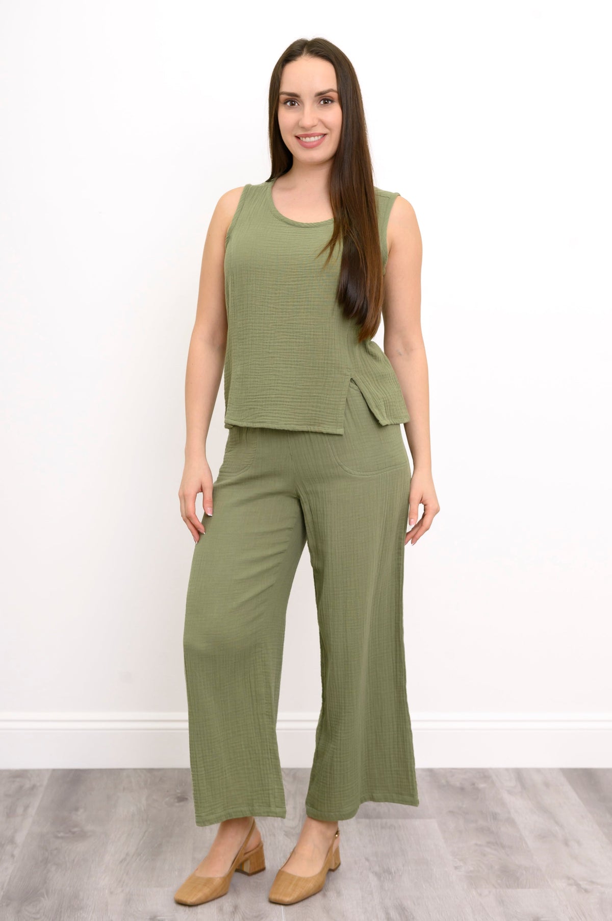 Woman wearing a green sleeveless top, wide-leg pants against, and tan shoes against a white background, front view