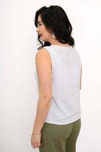 Woman wearing a white sleeveless top and green pants on a white background, back view