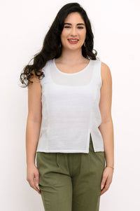Woman wearing a white sleeveless top and green pleated pants on a white background, front view