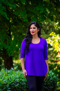 Woman outdoors wearing a vivid purple long sleeve shirt with curved hemline