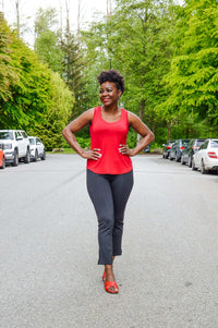 Woman outdoors wearing bright red tank top and black pants, hands on hips
