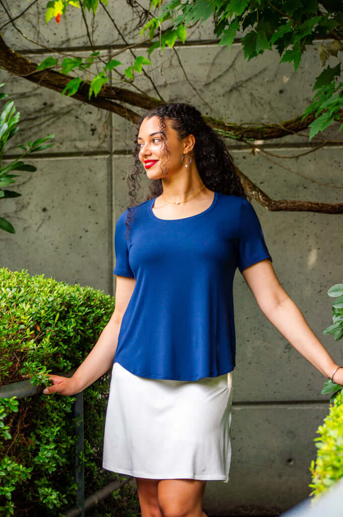 Woman in navy blue scoop neck tee and white skirt standing outdoors