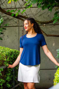 Woman in navy blue scoop neck tee and white skirt standing outdoors