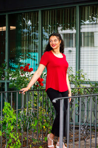 Woman in a crimson scoop neck tee with black pants, standing outdoors by a railing