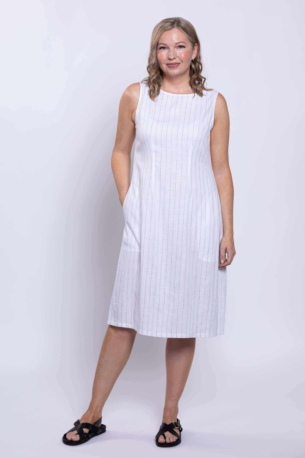 Woman standing in sleeveless white dress with vertical stripes and pockets