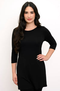 Close up front view of woman wearing long sleeve black tunic, smiling with her hand on her hip