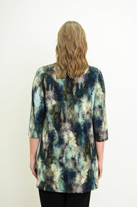 Rear view of a a female model wearing a blue-green watercolor forest print A-line tunic with 3/4 sleeves with black pants. Against a white backdrop
