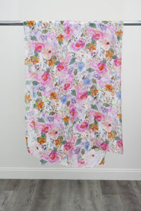 A large silk scarf with a pink and multicolour floral pattern displayed on a metal rod against a white background, front view